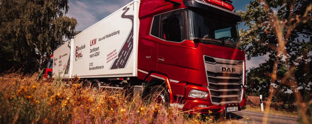 Ein moderner roter Schulungs-LKW der Fahrschule Flegel fährt auf einem Übungsgelände in der Region Walsrode/Celle unter blauem Himmel.