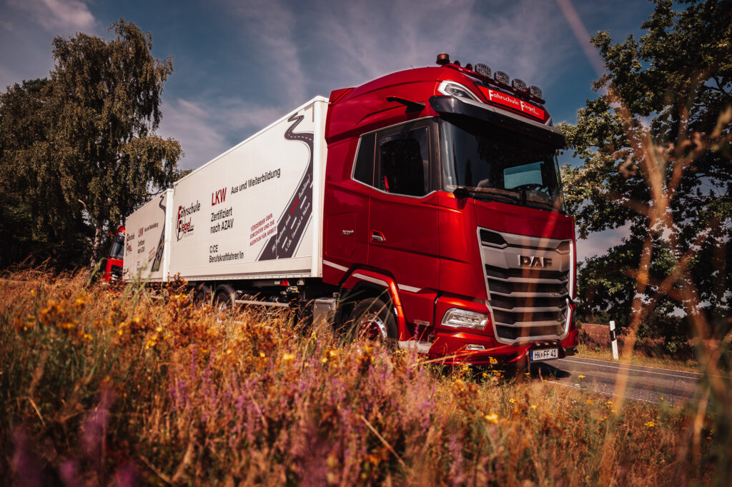 Ein moderner roter Schulungs-LKW der Fahrschule Flegel fährt auf einem Übungsgelände in der Region Walsrode/Celle unter blauem Himmel.